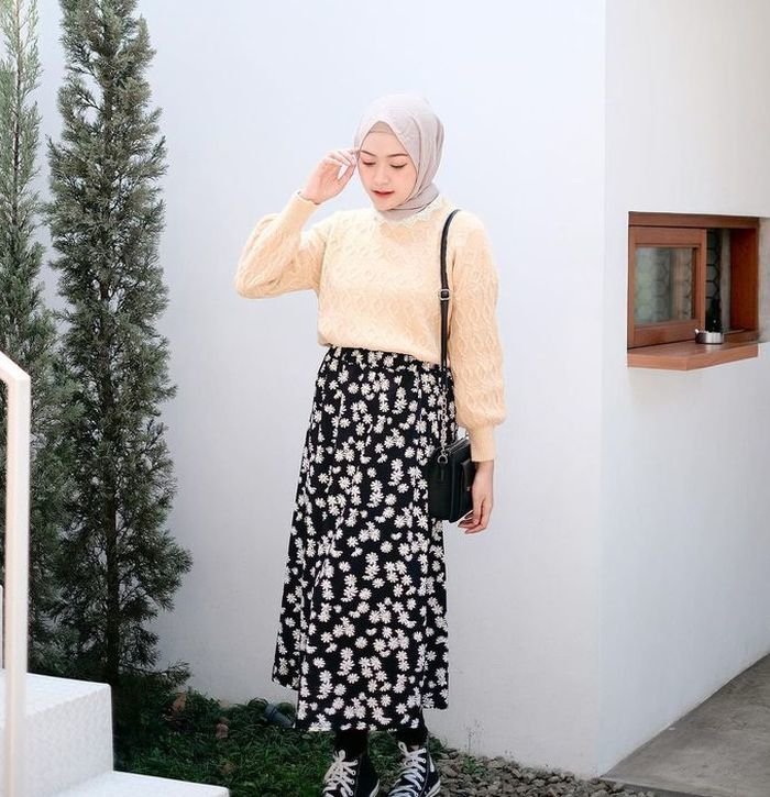 Wanita Indonesia berhijab mengenakan atasan sweater warna beige dan rok panjang motif floral.